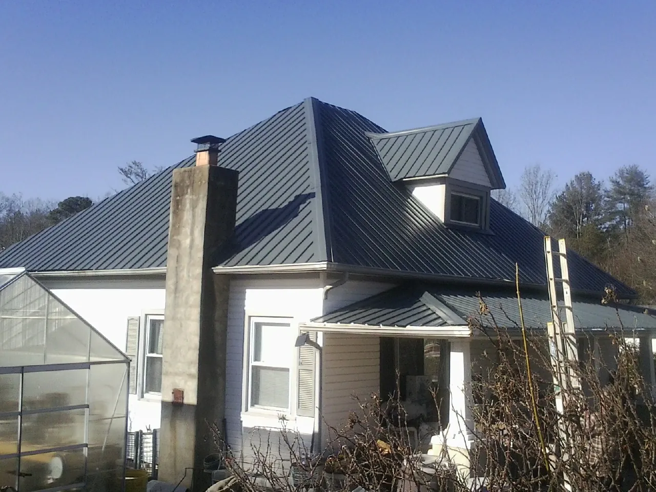 Dark blue standing seam metal roof on a white farmhouse with dormer — Slate & Tile Roof Repair by Roofing Brothers in Ellis