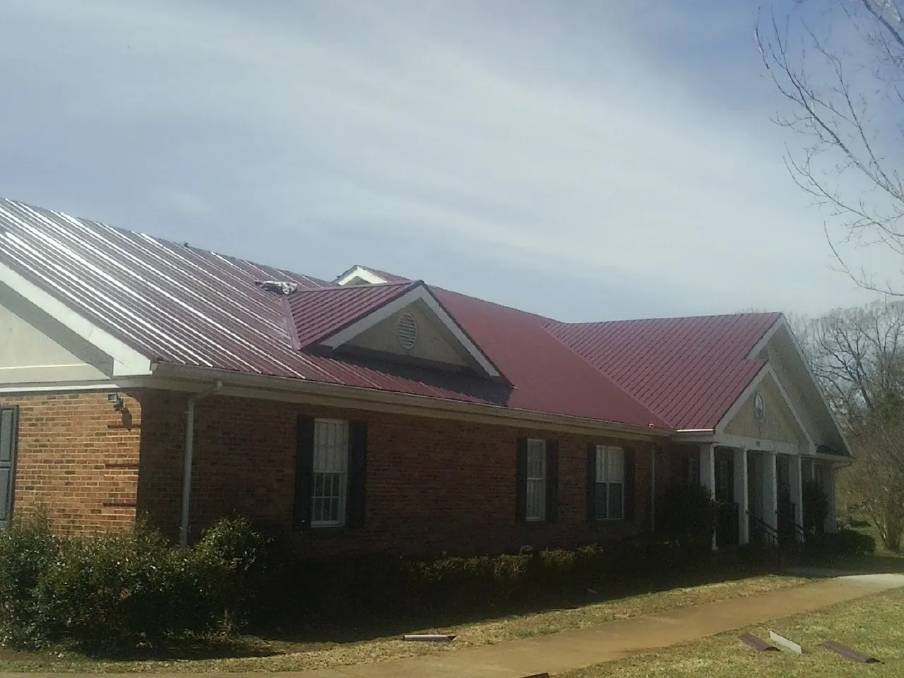 Red metal roof with gabled entries on a long brick building, from a Hail Damage Roof Repair job in Ellis