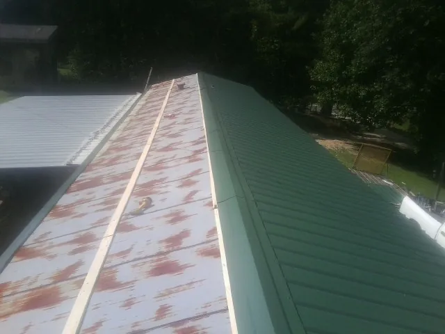 Old rusted panels beside newly installed green metal roofing — Wind Damage Roof Repair by Roofing Brothers in Ellis
