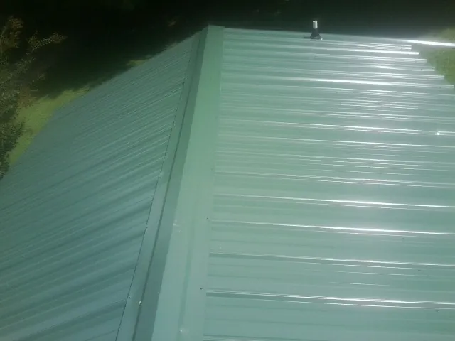 New green metal panels meeting at the ridge of a roof — Flat Roof Repair work by our crew in Ellis