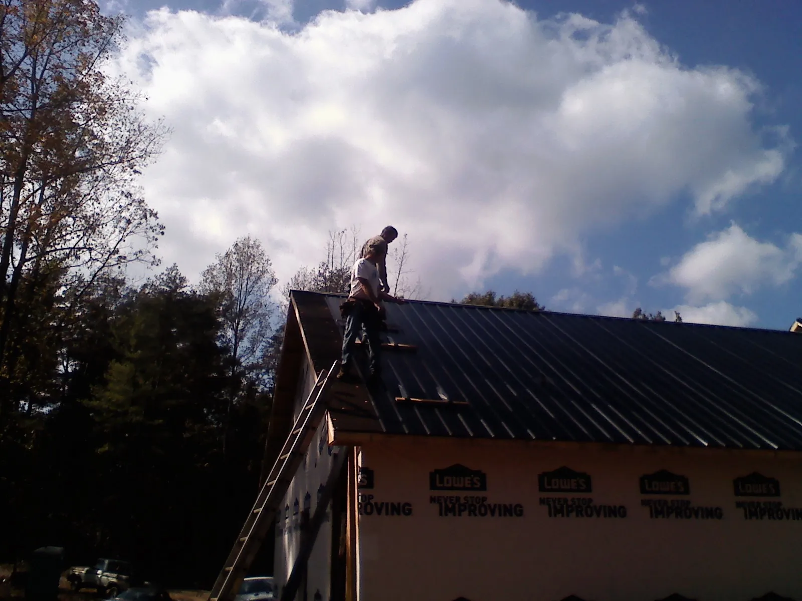Roofer fastening dark metal panels high against a cloudy sky, from a Roof Inspection job in Ellis