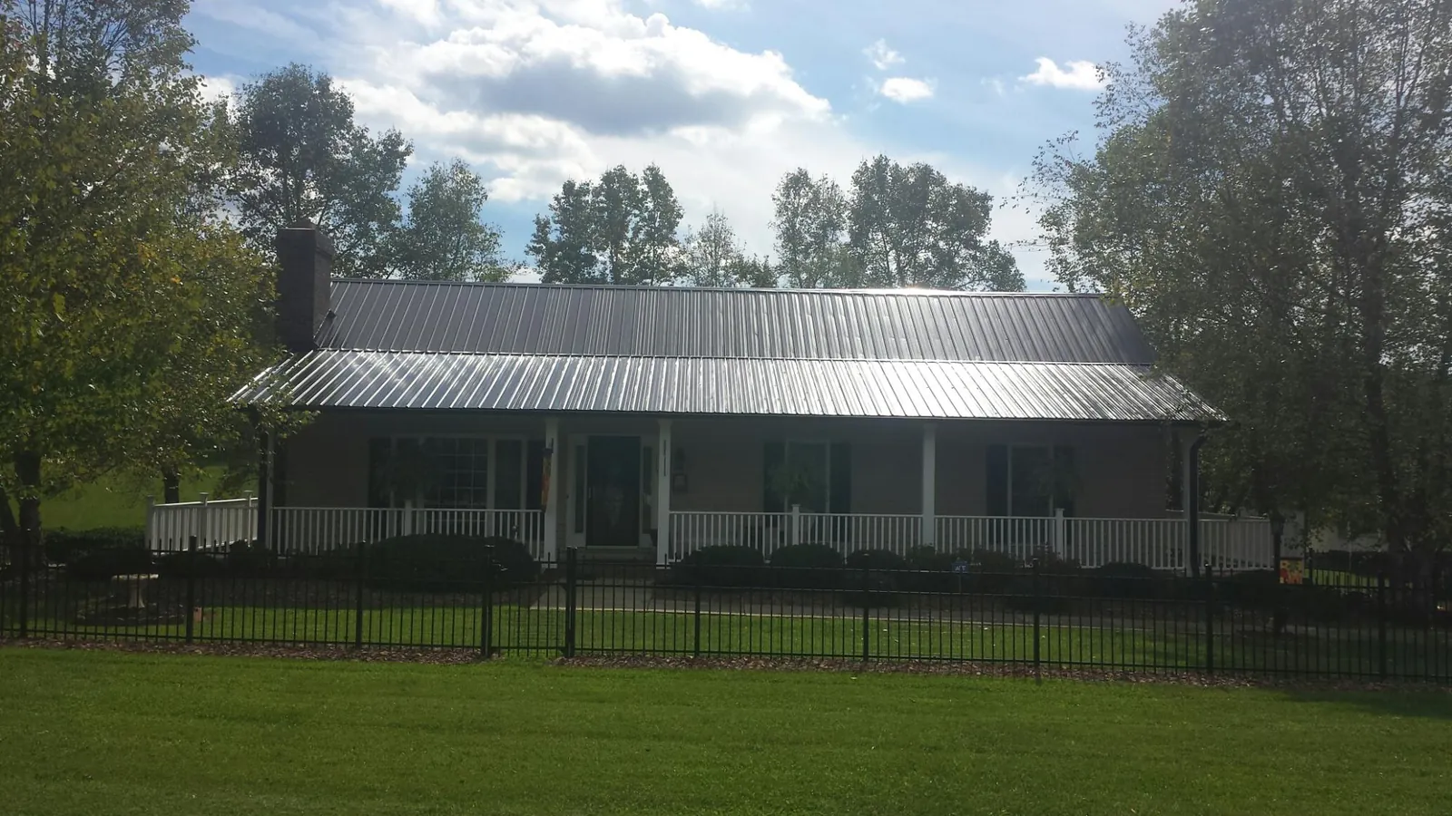 Gray metal roof on a brick ranch with a full width front porch — Gutter Guard Installation work by our crew in Ellis