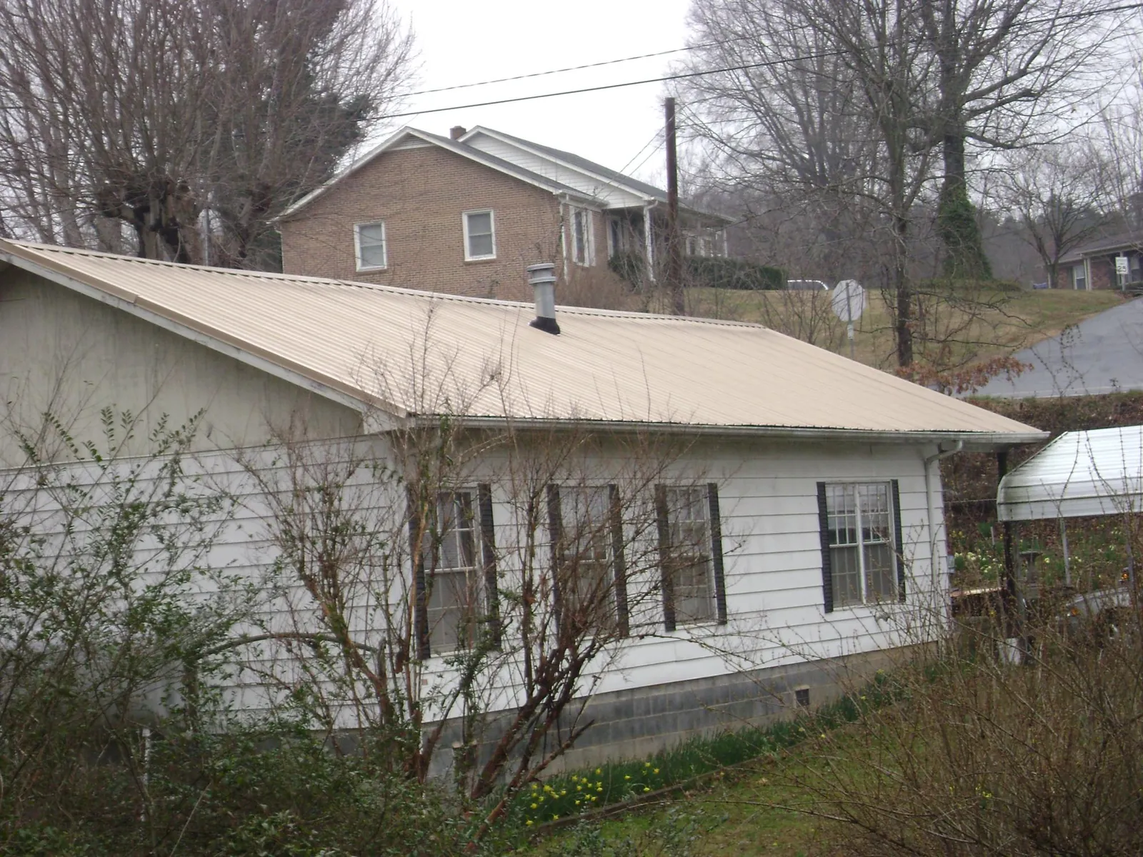 Tan metal roof on a white sided house set into a hillside — Commercial Roofing by Roofing Brothers in Ellis