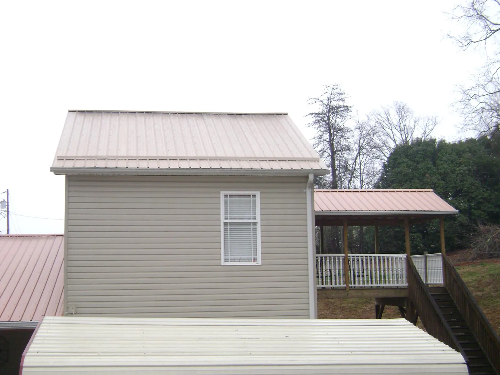 Tan metal roofs on a two story addition and attached porch, from a Roof Replacement job in Ellis